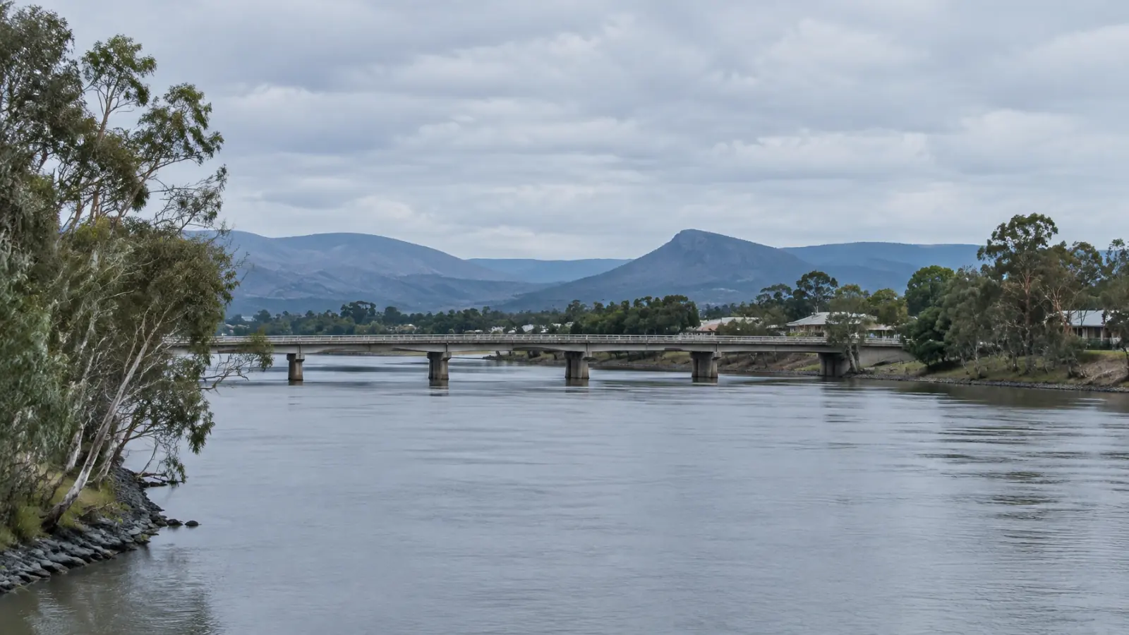 A quiet Central Queensland riverfront townscape with a low bridge and layered hills