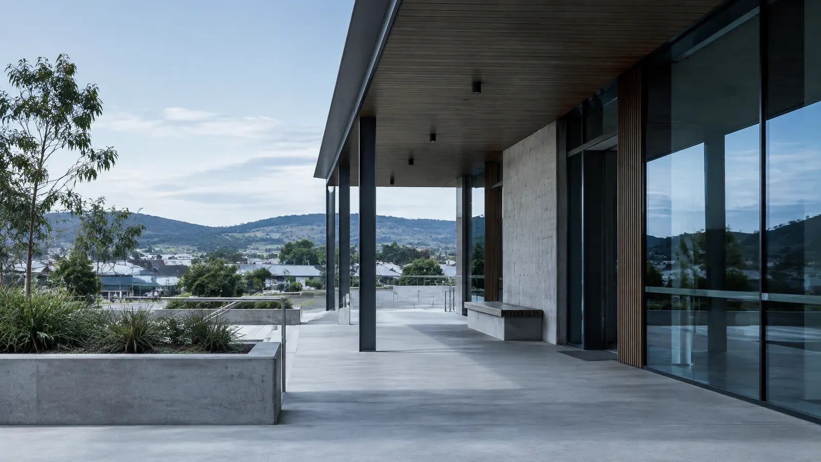 A quiet regional building with concrete, glass, and a shaded verandah framed by low hills