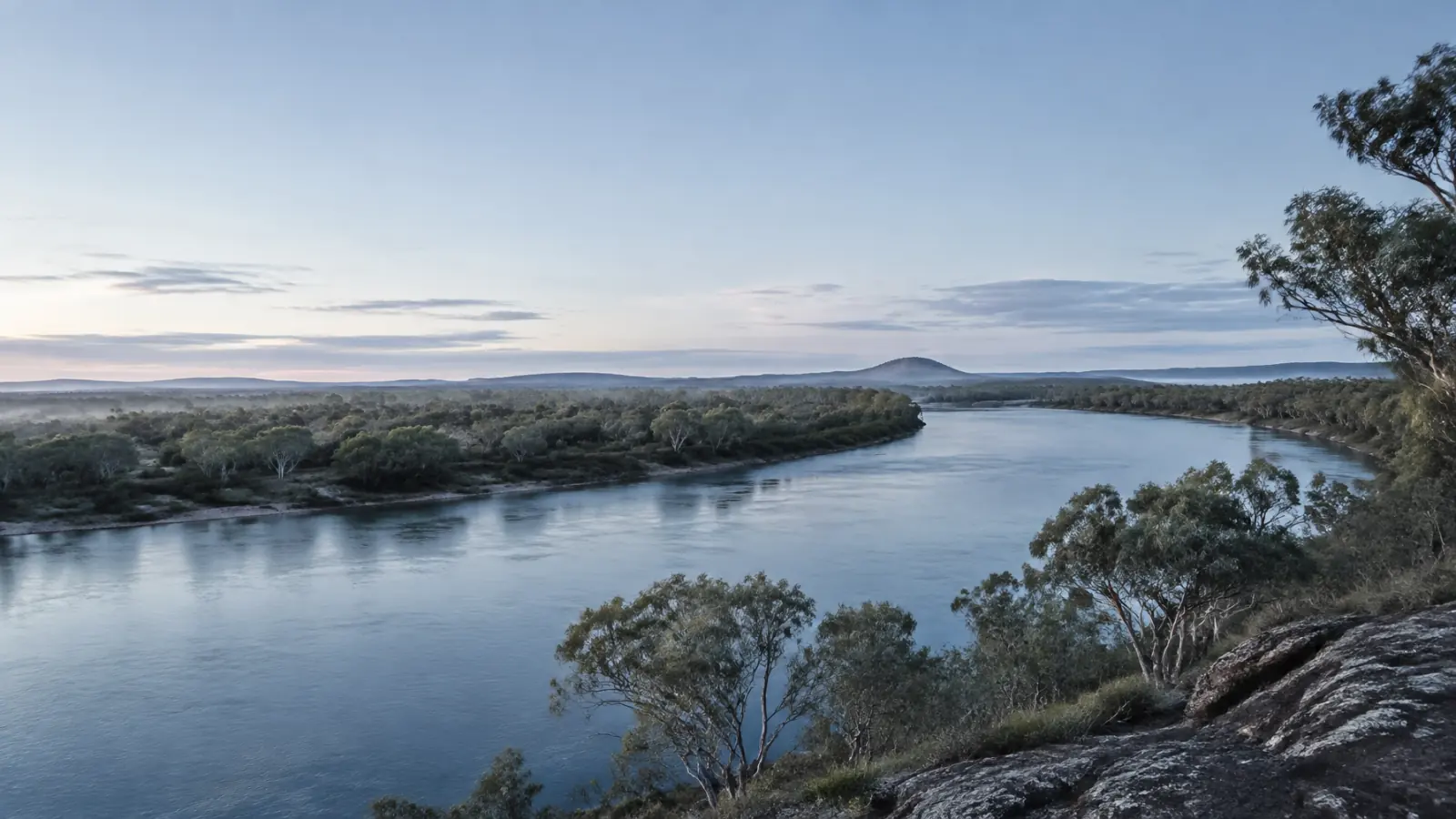 A broad Central Queensland river bend beneath low hills and eucalyptus trees